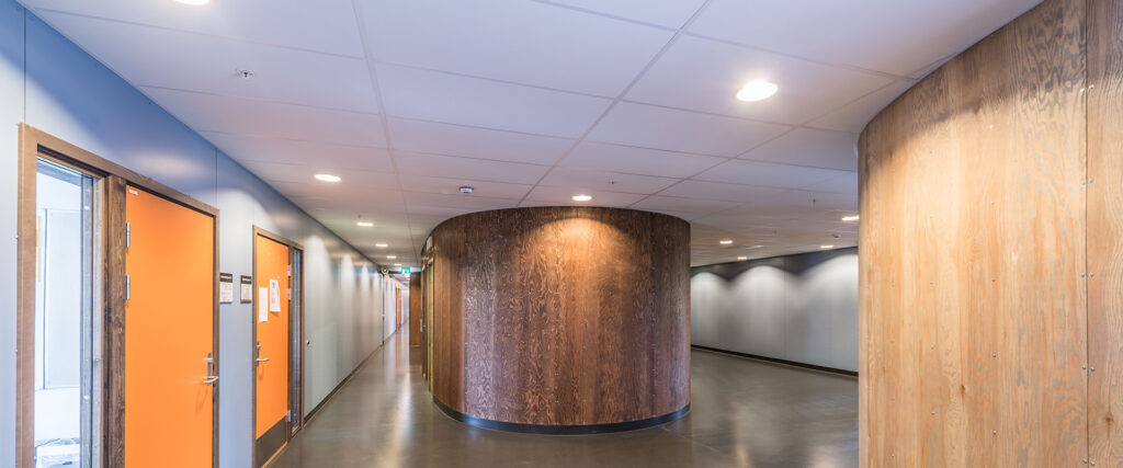 Korridor med infällda rundade downlights från PROLJUS AB som levererar jämnt bländfritt LED-ljus och framhäver träpanelernas struktur, energieffektiva armaturer för moderna offentliga miljöer