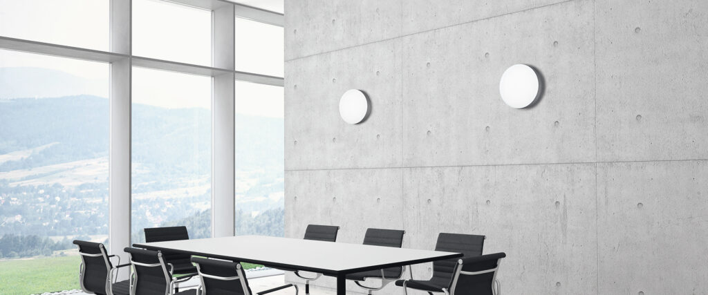 Två runda LED-väggarmaturer på betongvägg i ett modernt konferensrum som sprider mjukt, energieffektivt arbetsljus och framhäver elegant design från PROLJUS AB