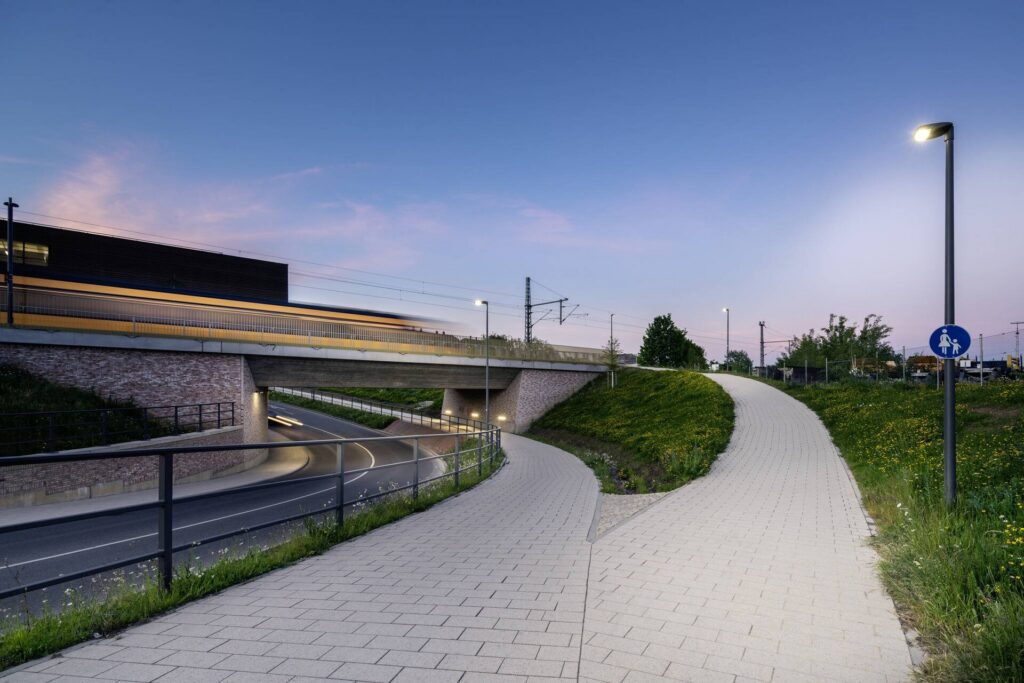 Kvällsbild av väg och gångbana vid viadukt belyst av PROLJUS ABs moderna, energieffektiva LED‑stolparmaturer som ger jämnt, bländfritt ljus och ökad trygghet och visuell attraktionskraft för offentliga miljöer