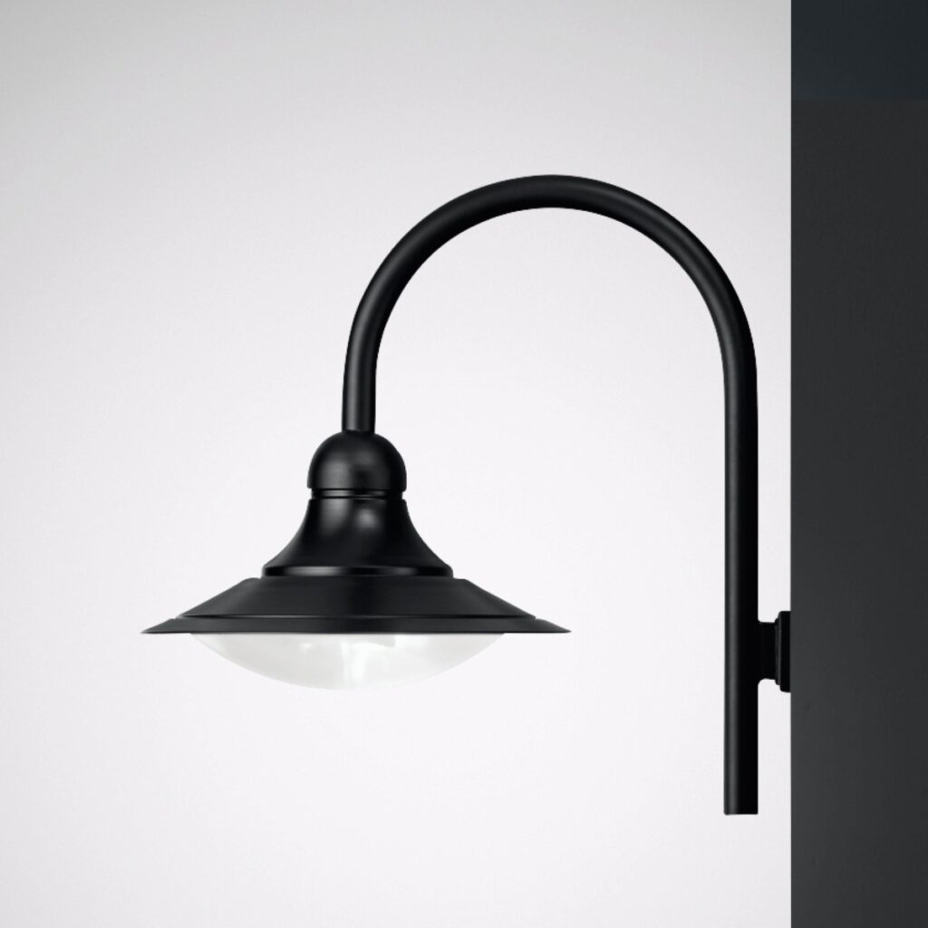 Svart matt väggarmatur med bågformad arm och platt klockskärm över opalvit kupol som ger mjukt nedåtriktat sken, perfekt för fasad- och entrébelysning från PROLJUS AB