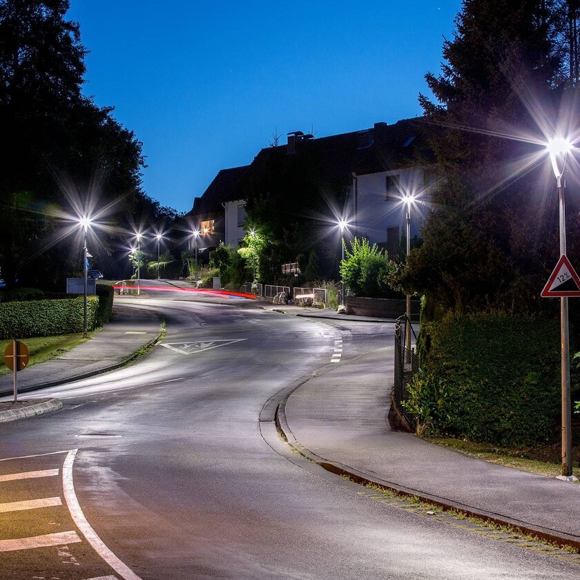 Kurvig kvällsgata upplyst av PROLJUS AB:s moderna, energieffektiva gatlyktor som sprider klart, jämnt vitt ljus med stjärnliknande strålglans och ökar trygghet samt fastighetsvärde