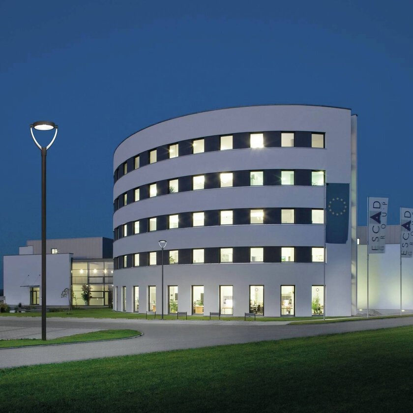 PROLJUS AB LED-armaturer i förgrunden lyser upp en modern rund kontorsbyggnad i skymning med jämn energieffektiv belysning som framhäver fasaden och skapar trygg och inbjudande utomhusmiljö för kommersiella projekt