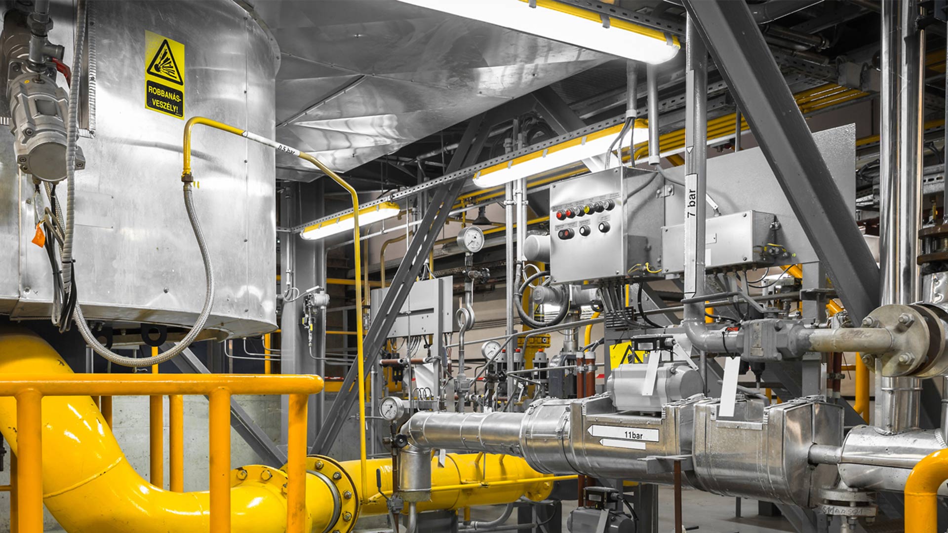 Industriell produktionsmiljö med långa linjära LED-armaturer monterade i tak och över maskiner som ger klart kallvitt, bländfritt ljus och visar PROLJUS AB:s robusta, energieffektiva belysningslösningar för säkra och effektiva arbetsytor