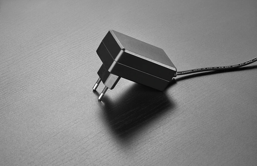 Svart kompakt nätadapter med två rundstift och kabel på mörk yta, en pålitlig strömlösning för PROLJUS ABs armaturer