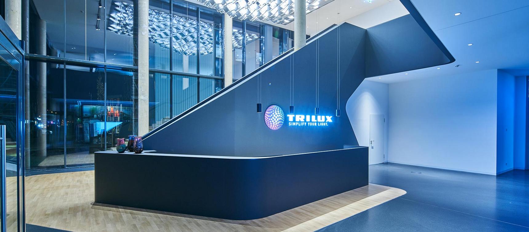 Stilren kontorslobby med upphängda cylindriska LED-pendlar och reflekterande takmoduler som ger ett jämnt, kallt blåvitt ljus över en minimalistisk receptionsdisk, ett övertygande säljexempel på PROLJUS ABs belysningslösningar som kombinerar modern design och energieffektivitet