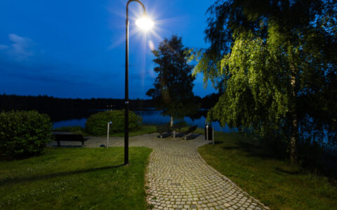 Gatlykta från PROLJUS AB lyser klart över en kullerstensstig vid sjö i skymning och demonstrerar en energieffektiv modern parkarmatur som skapar trygghet och stämning