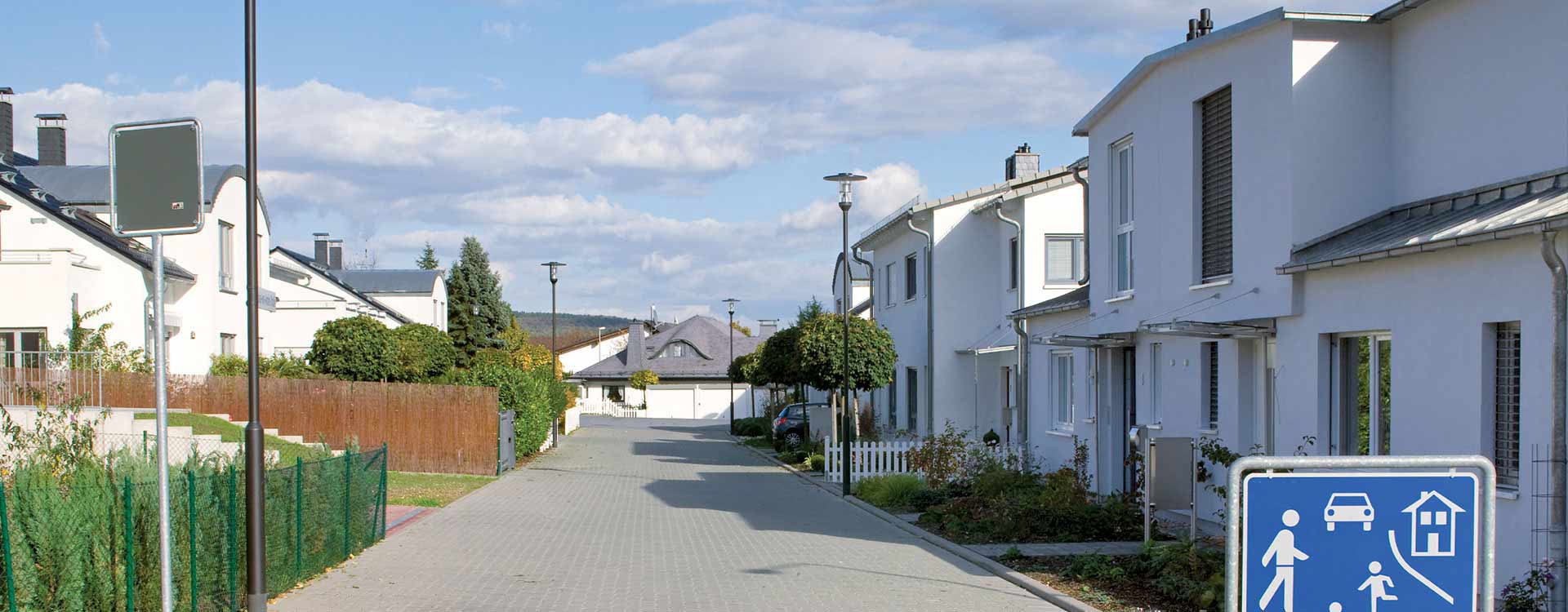 Slanka moderna gatarmaturer monterade på stolpar längs en bostadsgata som ger jämn, bländfri och energieffektiv belysning som framhäver fasaderna och skapar trygghet kvällstid, högkvalitativa och lättinstallerade lösningar från PROLJUS AB