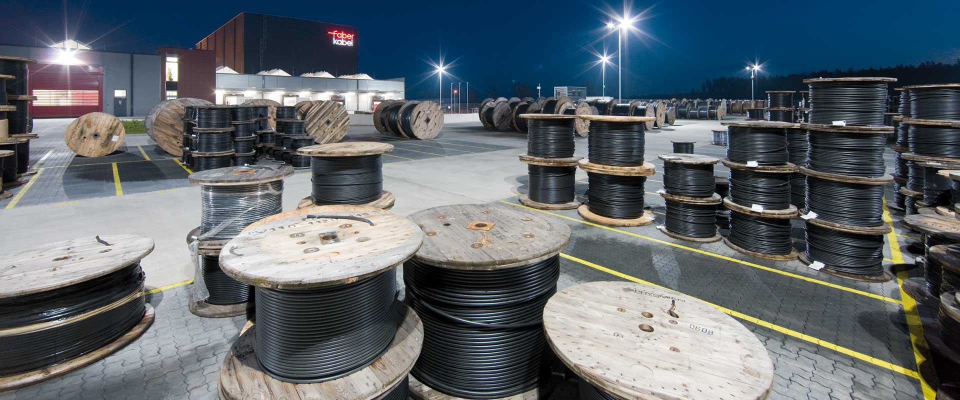 Industrigård på natten med flera kraftfulla LED-armaturer som skapar skarpt, jämnt och energieffektivt ljus över lagerområdet och kabeltrummor, ett bevis på PROLJUS ABs utomhusbelysning för ökad säkerhet och lägre driftskostnader