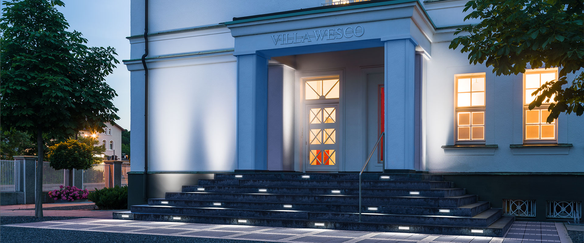 Entré trappa där infällda LED-armaturer i varje trappsteg ger jämn och säker stegmarkering samt dekorativ kallvitt accentbelysning, ett stilrent referensprojekt som visar PROLJUS AB:s energieffektiva och högkvalitativa utomhusarmaturer