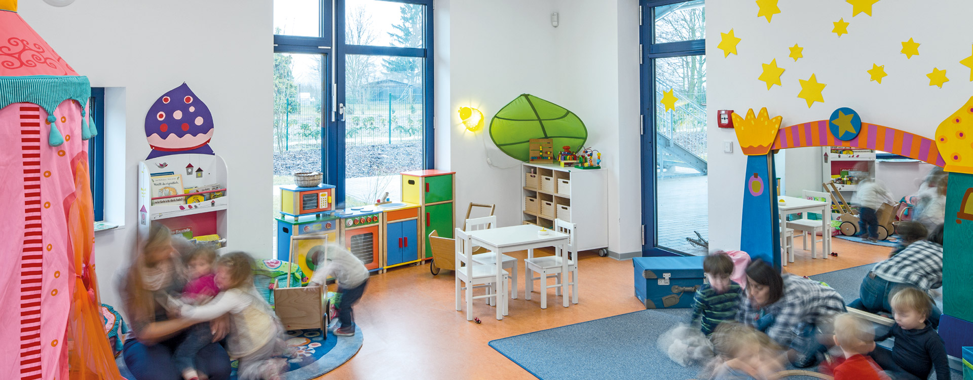 Förskolerum med stora fönster och två dekorativa väggarmaturer från PROLJUS AB en varm gul solformad lampa och en mjukt upplyst grön lövformad lampa som skapar tryggt, energieffektivt och barnvänligt ljus perfekt för daghem och skolor