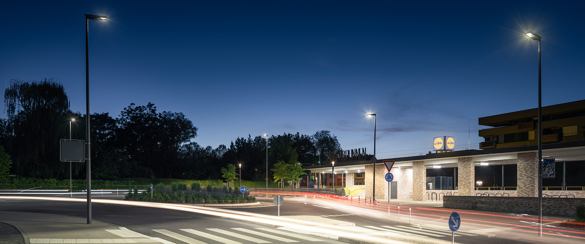 Nattvy över rondell och gata belyst av PROLJUS ABs moderna, energieffektiva LED-armaturer på slanka stolpar som kastar jämnt, bländfritt ljus över körbana, övergångsställe och trottoar och framhäver säkrare trafikrörelser och attraktiv utomhusmiljö