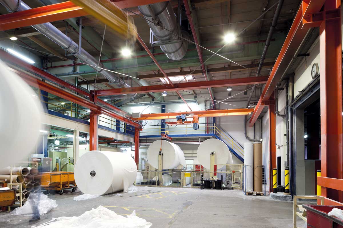 Industrilokal upplyst av kraftfulla PROLJUS AB LED‑armaturer monterade i takets stålbalkar, jämn och bländfri högbelysning som framhäver maskiner och stora pappersrullar, energieffektiva och robusta lösningar för krävande miljöer som minskar driftkostnader och underlättar installation