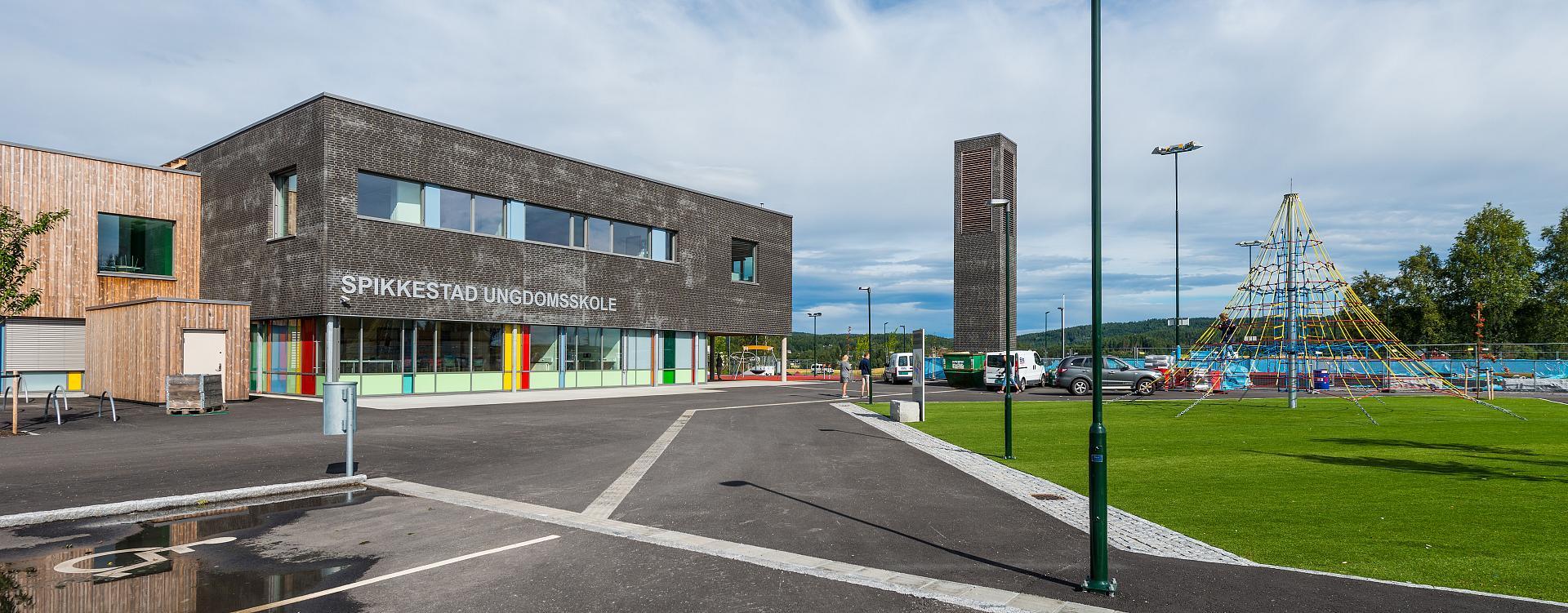 Skolområde och lekplats i dagsljus med flera moderna mörkgröna gatlyktor från PROLJUS AB som erbjuder energieffektiv LED-belysning, jämn ljusfördelning, robust och vandalresistent konstruktion samt stilren design idealisk för skolor och offentliga miljöer