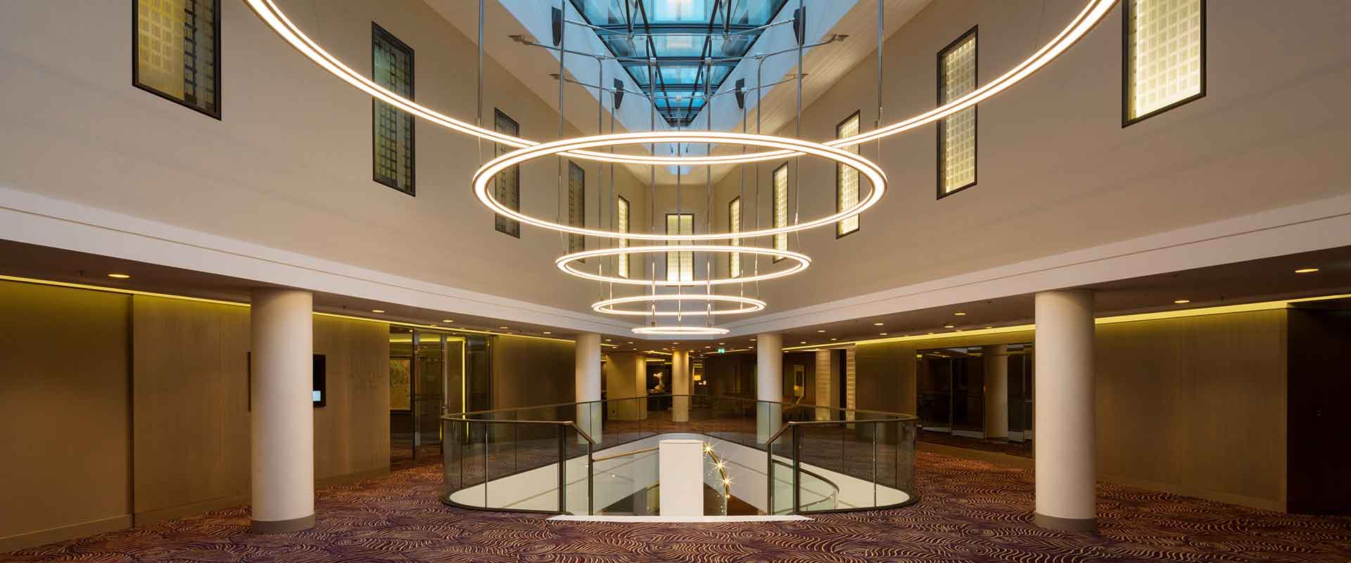 Modern entréhall med flera hängande cirkulära ljusringar i serie som skapar varm, jämn och dekorativ belysning, en elegant och energieffektiv armatur från PROLJUS AB