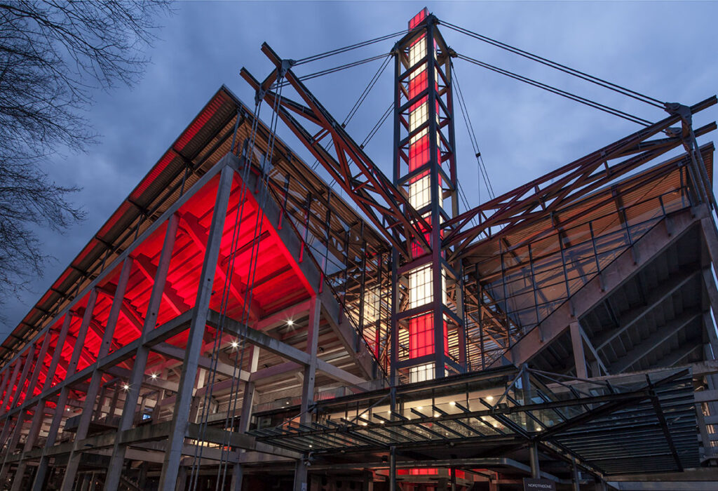 Rött och varmvitt LED-ljus från PROLJUS AB belyser arenans stålkonstruktion, framhäver pelare, trappor och torn och skapar dramatisk, energieffektiv projektbelysning perfekt för arenor och offentliga byggnader