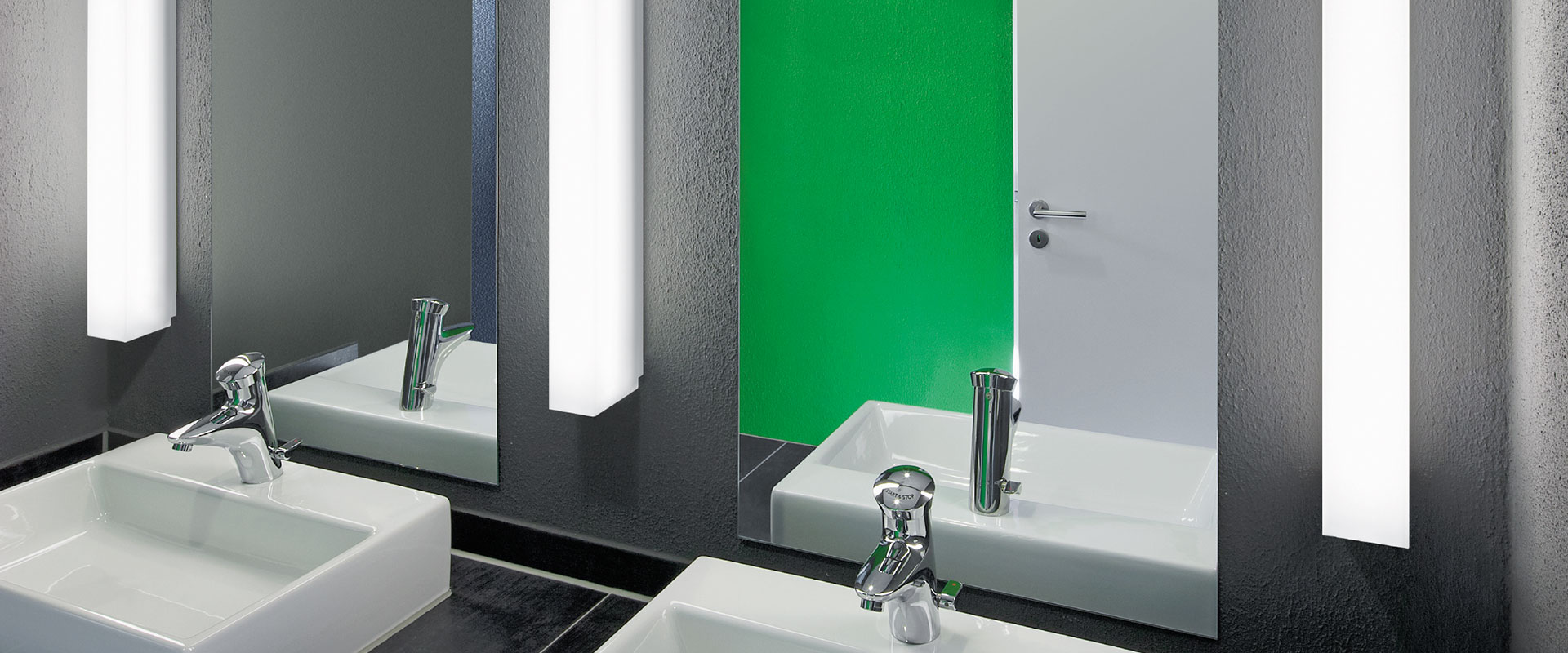 Modernt badrum med speglar och två slanka rektangulära väggarmaturer från PROLJUS AB som avger mjukt, jämnt och energieffektivt ljus över handfaten, stilren design som passar både professionella och privata miljöer