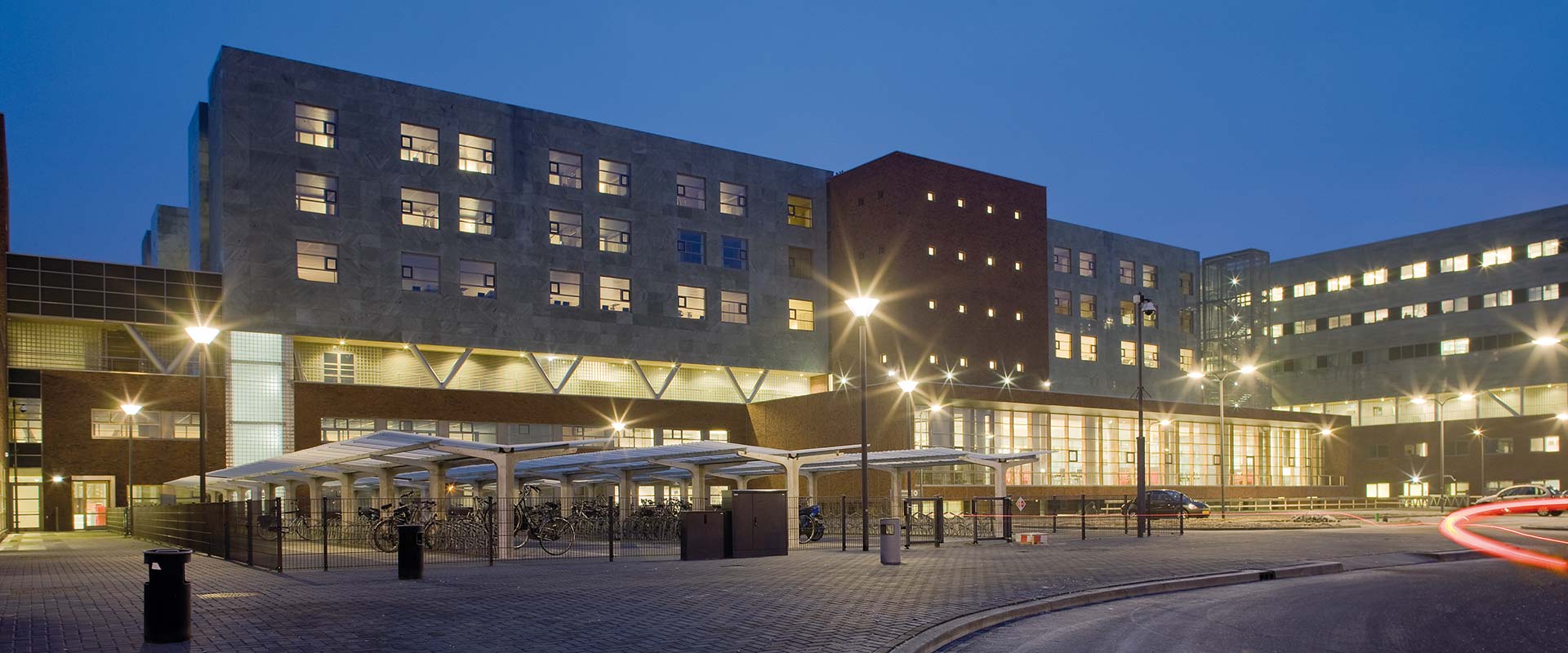 Nattbild av en modern kontorsbyggnad upplyst av flera PROLJUS AB-gatlyktor och fasadarmaturer som skapar stjärnliknande ljuseffekter och jämn varm LED-belysning, en energieffektiv lösning för trygg och attraktiv utomhusbelysning