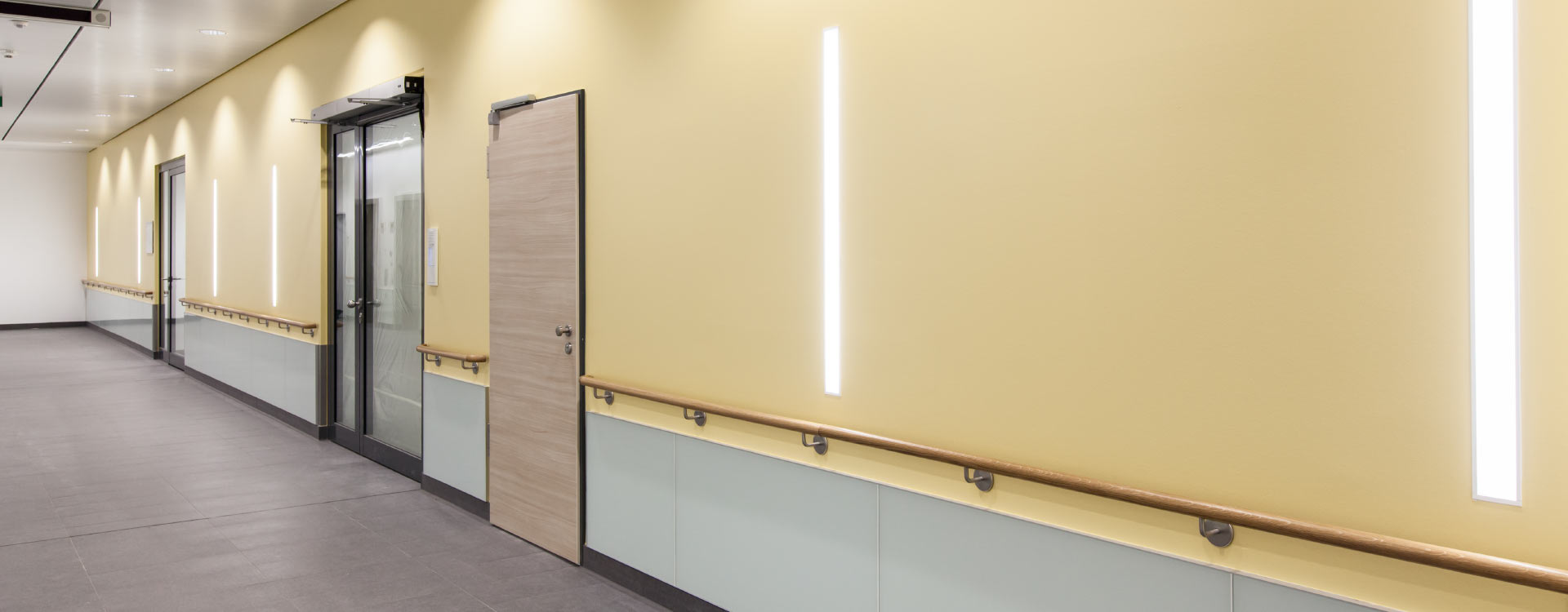 Korridor belyst av slimmade vertikala LED-ljuslister som ger jämnt, varmt ljus och ökad trygghet, energieffektiva och eleganta armaturer från PROLJUS AB idealiska för vård och offentlig miljö
