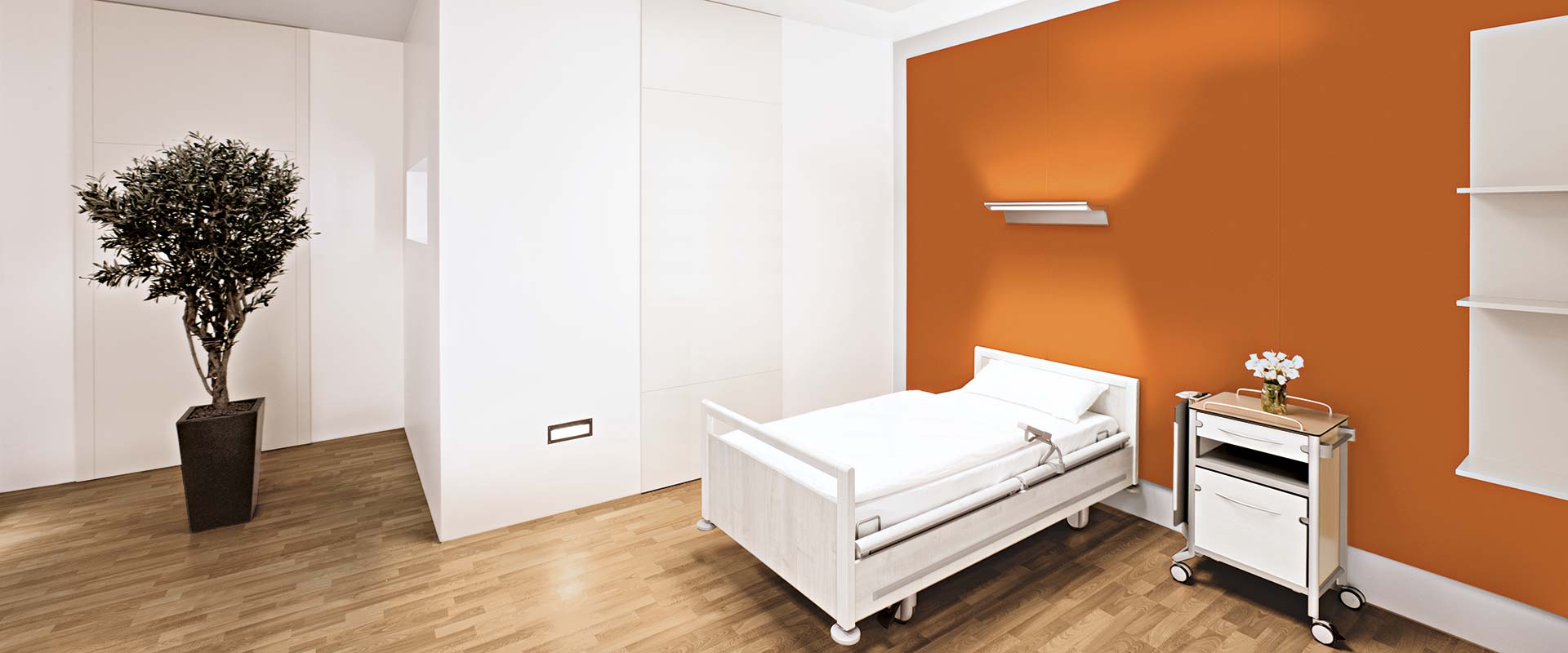 Modern väggarmatur från PROLJUS AB monterad ovanför sjukhussäng som sprider varmt upp- och nedåtriktat ljus tillsammans med diskret infälld belysning vid golvnivå, stilren och funktionell belysning perfekt för vård- och patientrum