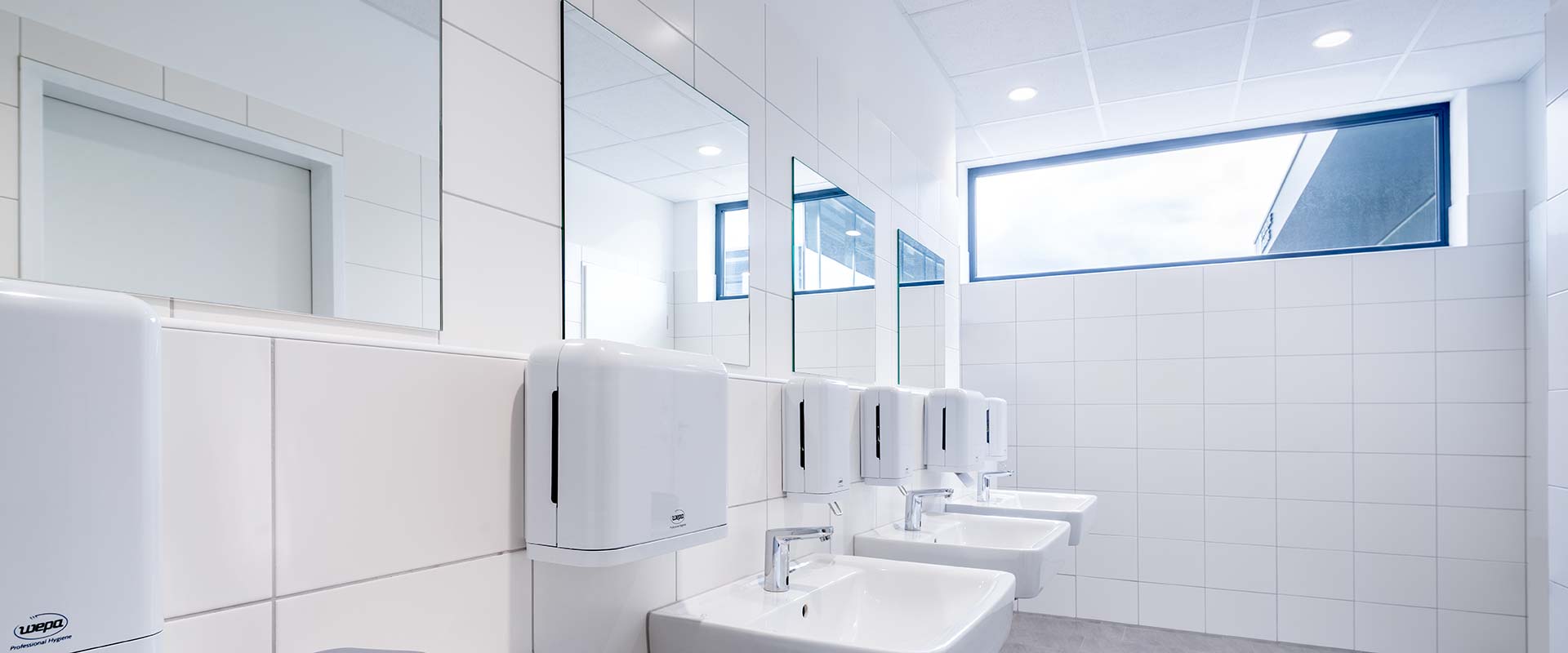 Infällda LED-armaturer i taket ger klart, jämnt och bländfritt ljus i ett modernt offentligt handfatrum, energieffektiva och stilrena belysningslösningar från PROLJUS AB som förbättrar hygien, framhäver design och minskar driftkostnader