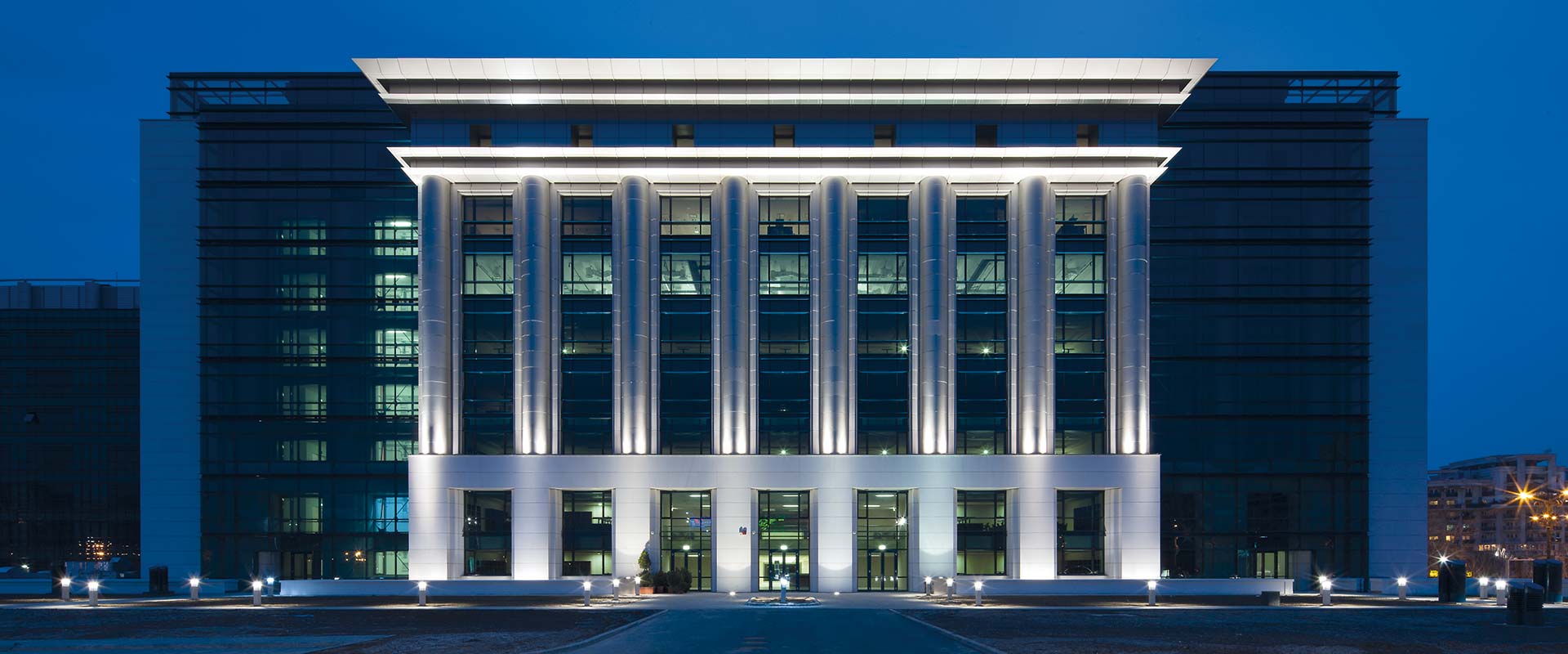 Modern kontorsfasad kvällstid belyst av PROLJUS AB:s LED-armaturer som framhäver vertikala pelare och entré, skapar dramatisk och energieffektiv fasadbelysning som ökar synlighet och prestige för kommersiella fastigheter