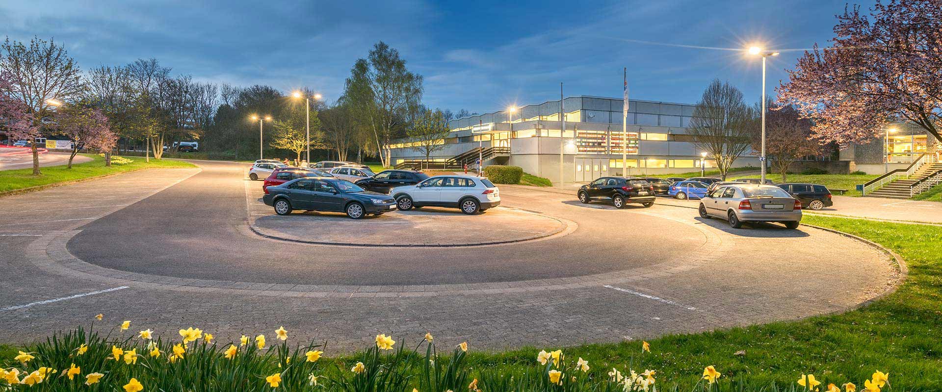 Kvällsbild av upplyst parkering och byggnad med jämnt spridda, moderna och energieffektiva gatlyktor och armaturer som skapar trygghet och god sikt, ett tydligt exempel på belysningslösningar från PROLJUS AB