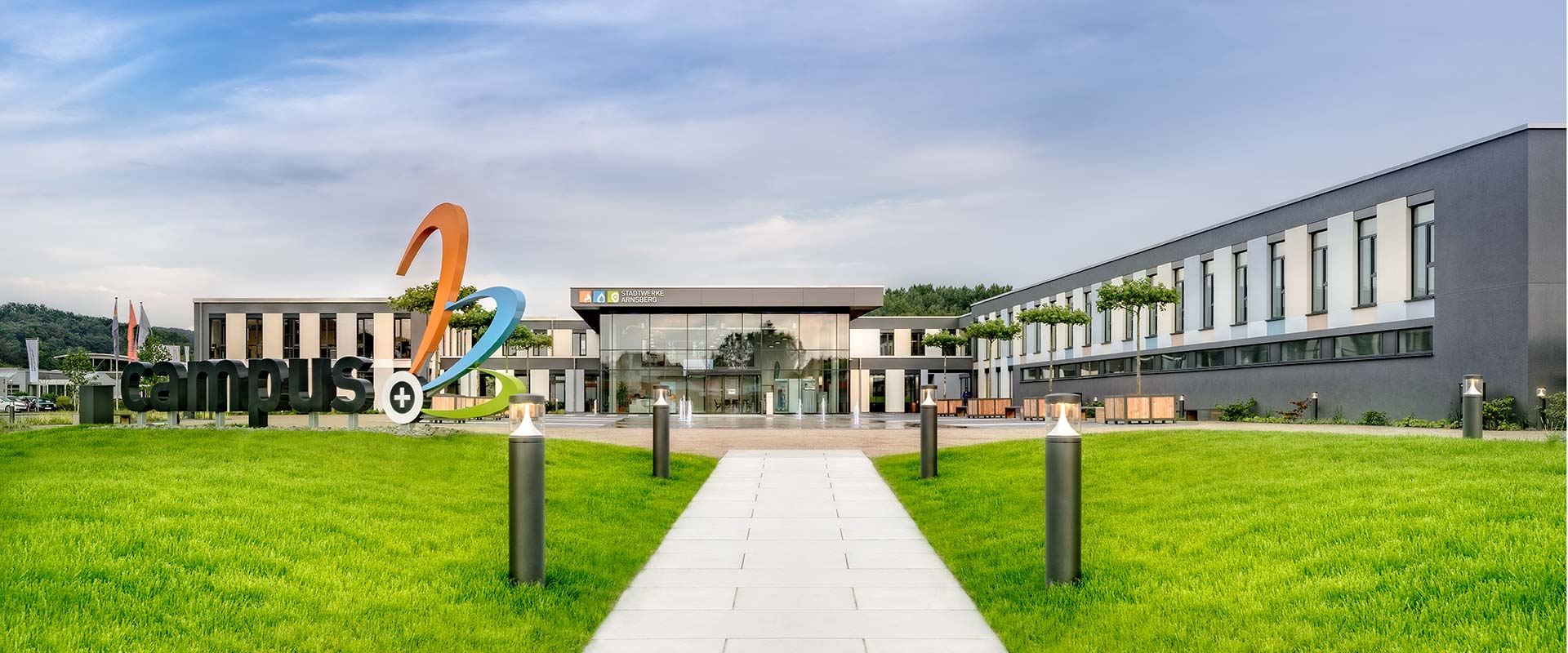 Gångstig till modern campusentré kantad av slimmade pollarlampor från PROLJUS AB som levererar energieffektiv, trygg och stilren utomhusbelysning för offentliga och privata miljöer