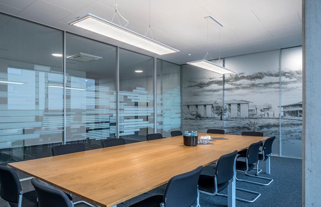 Konferensrum med långt ekbord och två upphängda, tunna rektangulära LED-armaturer från PROLJUS AB som ger jämnt, energieffektivt och bländfritt arbetsljus och framhäver modern kontorsdesign, idealiska för företag som vill uppgradera sin belysning
