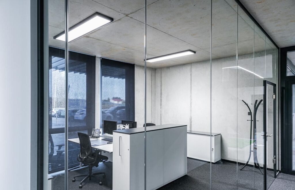 Rektangulära LED-takarmaturer från PROLJUS AB lyser upp ett modernt kontor med glasväggar och betongtak, ger jämnt, bländfritt arbetsljus, energieffektiv drift och en stilren estetik som höjer professionaliteten i mötesrum och öppna arbetsytor