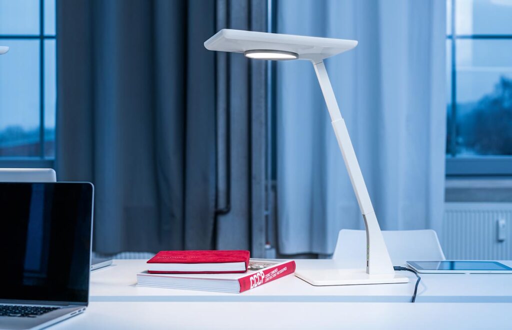 Vit modern LED-armatur från PROLJUS AB på skrivbordet med slimmad design och jämnt bländfritt arbetsljus som förbättrar fokus och förhöjer kontorsmiljön