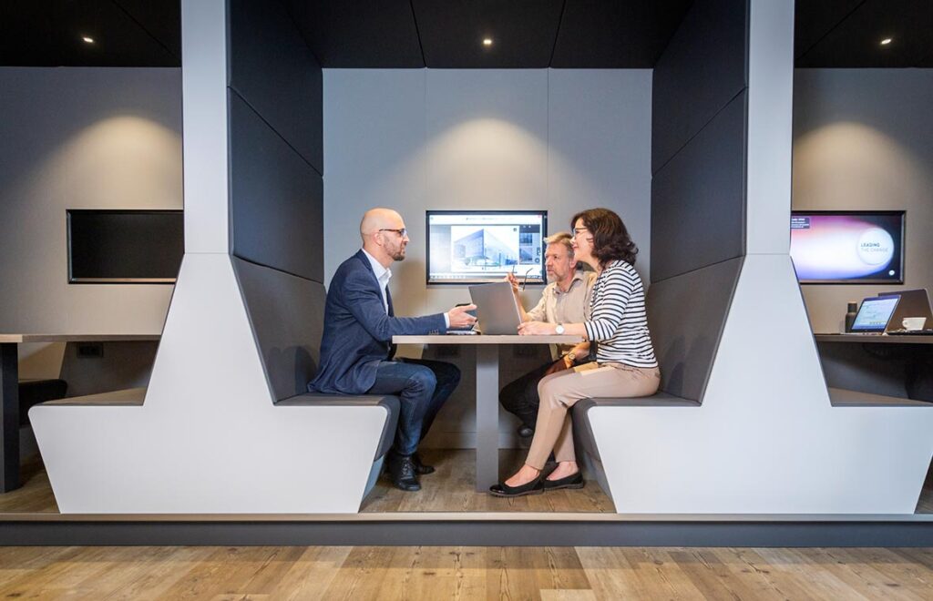 Tre personer i en modern mötesnisch belysta av diskreta infällda spotlights och jämnt arbetsljus som framhäver bord och ytor en säljande skräddarsydd armaturlösning från PROLJUS AB