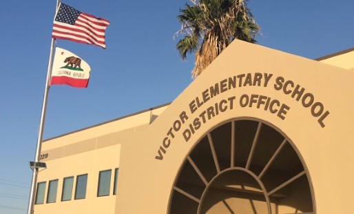 Fasad på Victor Elementary School med amerikansk och Kalifornienflagga, arkitekturen elegant framhävd av PROLJUS AB:s energieffektiva armaturer som skapar en trygg och inbjudande entré