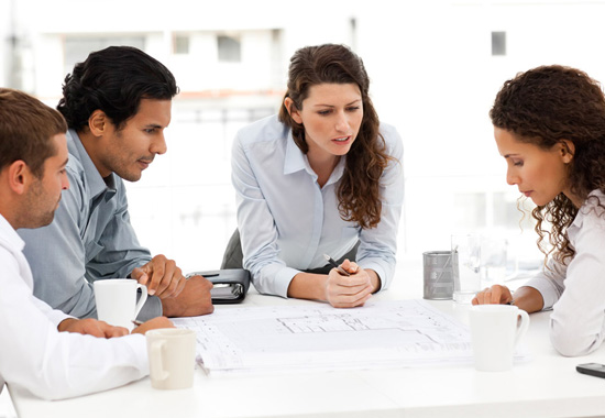 Fyra personer runt ett bord granskar ritningar i klart, jämnt ljus från PROLJUS AB:s energieffektiva armaturer som framhäver detaljer och ökar försäljningspotentialen