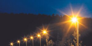 Rad av moderna gatlyktor i skymning med varmgult stjärnsken som jämnt belyser väg och träd, energieffektiva och attraktiva lösningar för offentliga miljöer från PROLJUS AB