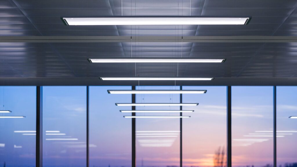 Rad av slimmade hängande linjära LED-armaturer i modern kontorsmiljö med stora fönster och varm kvällshimmel, energieffektiva med jämnt bländfritt ljus och elegant design från PROLJUS AB