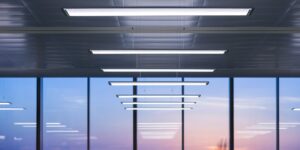 Rad av slimmade hängande linjära LED-armaturer i modern kontorsmiljö med stora fönster och varm kvällshimmel, energieffektiva med jämnt bländfritt ljus och elegant design från PROLJUS AB