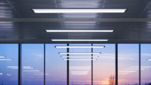 Rad av slimmade hängande linjära LED-armaturer i modern kontorsmiljö med stora fönster och varm kvällshimmel, energieffektiva med jämnt bländfritt ljus och elegant design från PROLJUS AB