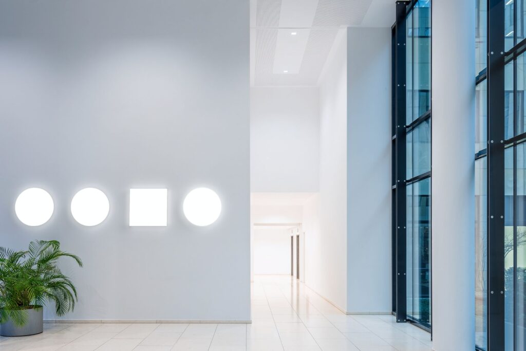 PROLJUS ABs väggarmaturer i entré med tre runda och en kvadratisk ljuspanel som avger mjukt vitt sken och skapar en elegant energieffektiv design för kontor och offentliga miljöer