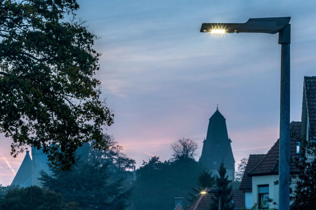 PROLJUS ABs moderna, energieffektiva LED-armatur på en gatlykta lyser klart över en småstad vid skymning, framhäver taksilhuetter och träd, perfekt för kommunala och privata belysningsprojekt