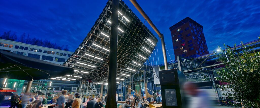 Stort utomhustak upplyst av rader med moderna LED-armaturer från PROLJUS AB som ger kraftfull, jämn och energieffektiv belysning över ett torg med sittplatser och folk, idealisk lösning för kommersiella evenemang och stadsrum