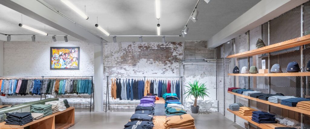 PROLJUS ABs belysning i en modern klädbutik med rörformade takarmaturer och riktbara spotlights som tydligt lyser upp hyllor och klädrackar och skapar en inbjudande atmosfär