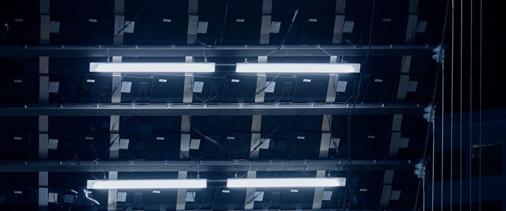 Närbild av linjära, energieffektiva lysarmaturer i kallvitt ljus monterade i metallram med synligt kablage och fästen, idealiska för industriella, scen- och kommersiella miljöer — PROLJUS AB erbjuder robusta, högpresterande belysningslösningar