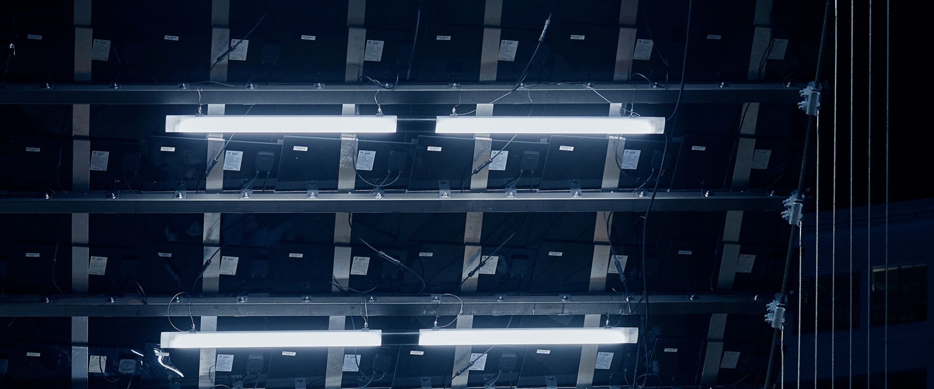 Närbild av linjära, energieffektiva lysarmaturer i kallvitt ljus monterade i metallram med synligt kablage och fästen, idealiska för industriella, scen- och kommersiella miljöer — PROLJUS AB erbjuder robusta, högpresterande belysningslösningar