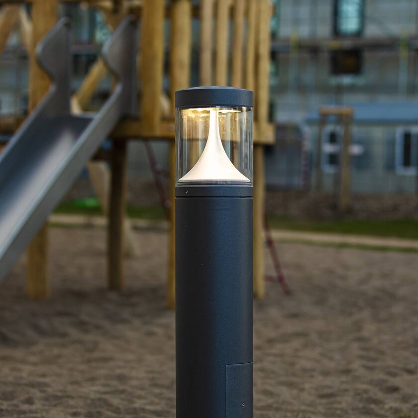 Elegant pollararmatur från PROLJUS AB i mörk metall med klart glasskydd och mjukt vitt LED-ljus, energieffektiv och robust lösning som ger säker och attraktiv belysning för parker och lekplatser