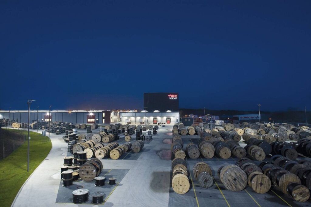 Nattvy över ett industriområde fullt av kabeltrummor upplysta av PROLJUS AB:s energieffektiva och robusta armaturer på höga stolpar som ger jämn, riktad belysning, ökad säkerhet och lägre energikostnader