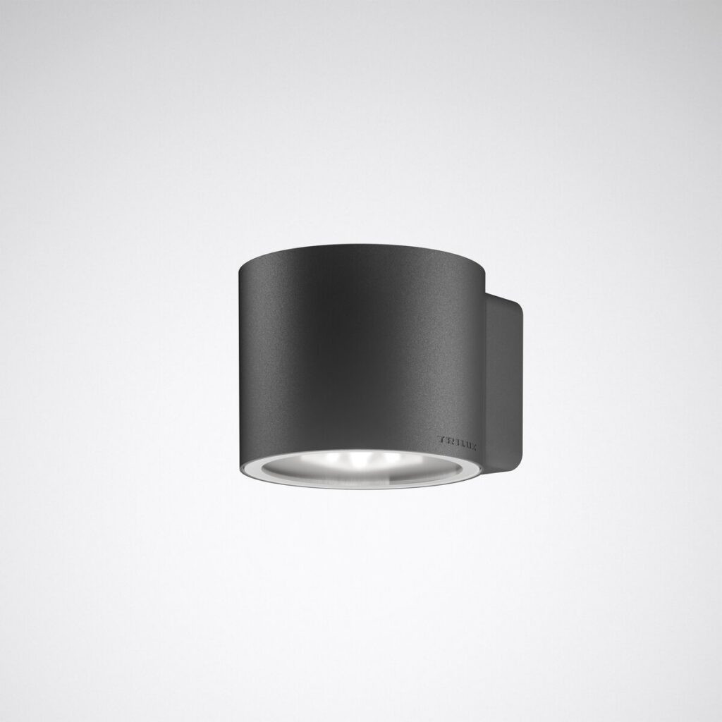 Mörkgrå cylindrisk väggarmatur i pulverlackerad metall med nedåtriktad LED-lins, energieffektiv och högkvalitativ minimalistisk design för entréer och fasadbelysning, säljs av PROLJUS AB