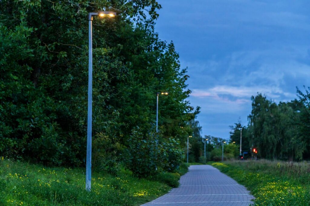 Gångväg i skymning upplyst av en rad moderna energieffektiva PROLJUS AB-luminärer på smala stolpar som ger jämn varm belysning, ökar tryggheten och tillför stilren design till parker och bostadsområden