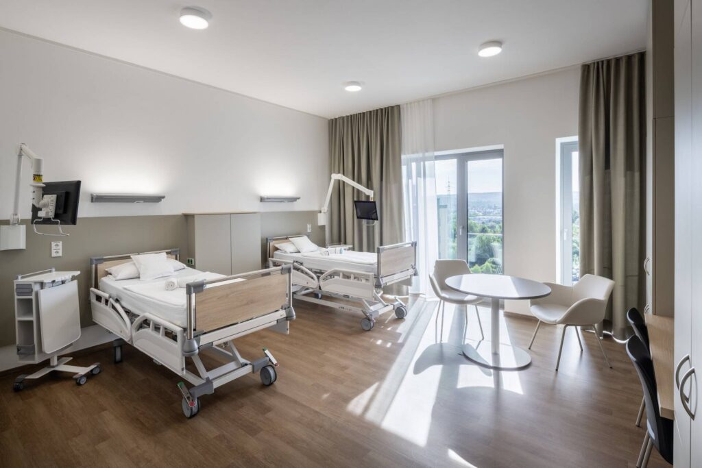 Vårdrum med två sjukhussängar upplysta av PROLJUS AB:s moderna, diskreta takarmaturer och vägglampor som ger jämnt, bländfritt och energieffektivt ljus för ett lugnt och professionellt intryck