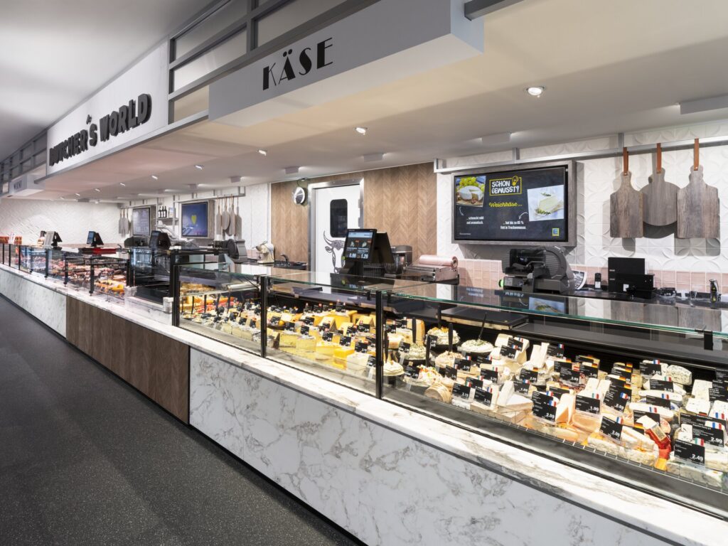 Modern butiksmiljö med PROLJUS AB:s infällda LED-downlights och spotlights som ger jämnt, varmt och färgäkta ljus över ost- och delikatessdiskar, framhäver texturer och färger, minskar energiförbrukningen och skapar en inbjudande, säljdrivande atmosfär för butiksägare som vill öka kundattraktion och försäljning