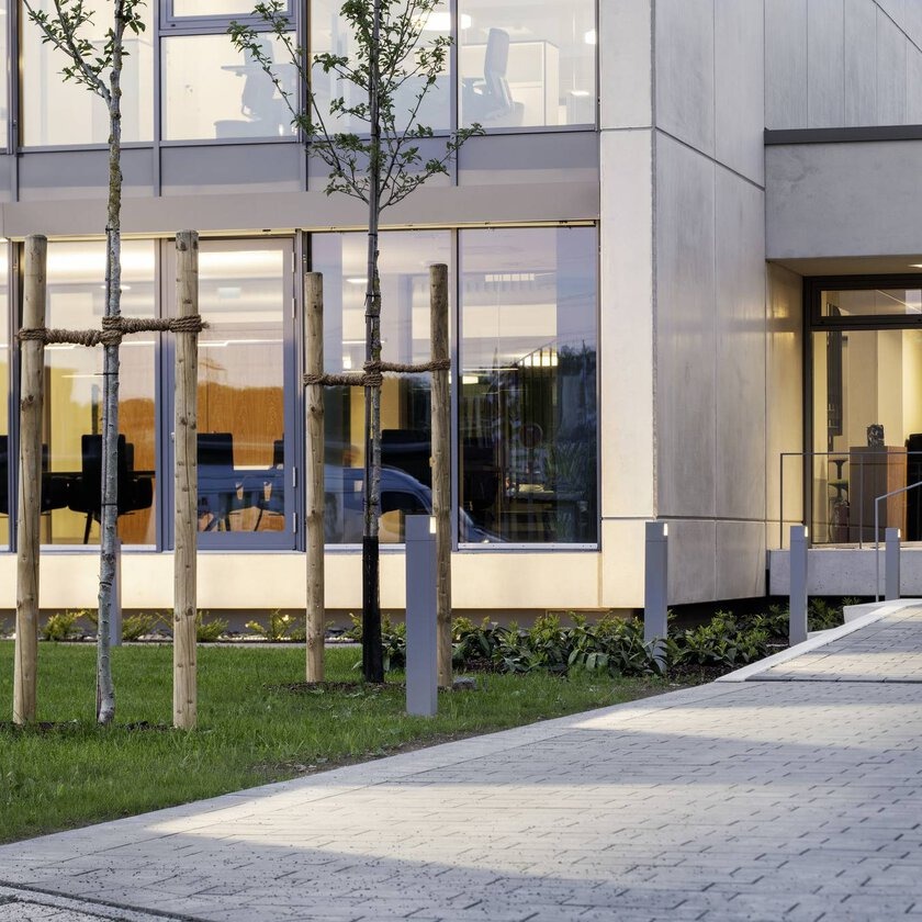 Elegant väderbeständig och energieffektiv pollarbelysning från PROLJUS AB som med varmvit nedåtriktad LED lyser upp gångväg och framhäver modern kontorsfasad i glas